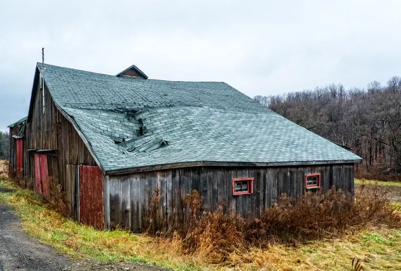 An old wooden barn with a caved-in metal roof